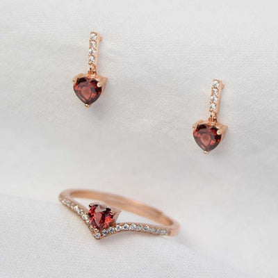 Image shows a close-up of the heart cut red garnet gemstones set in the earring and ring. The deep, rich red color of the garnet is highlighted by the surrounding metal setting.